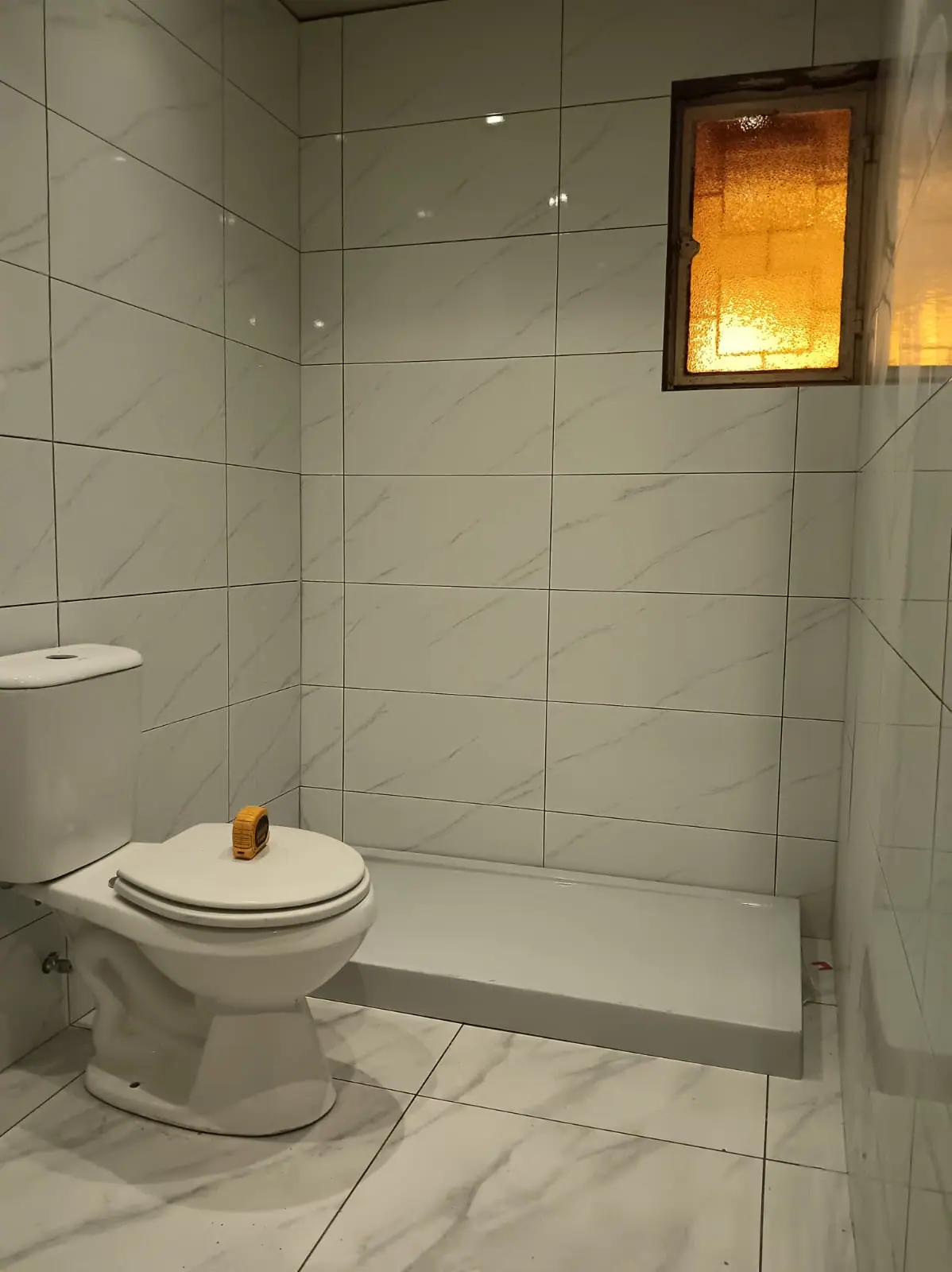 Baño terminado con porcelánico claro de gran formato, receptáculo de ducha a ras de suelo y artefactos nuevos.