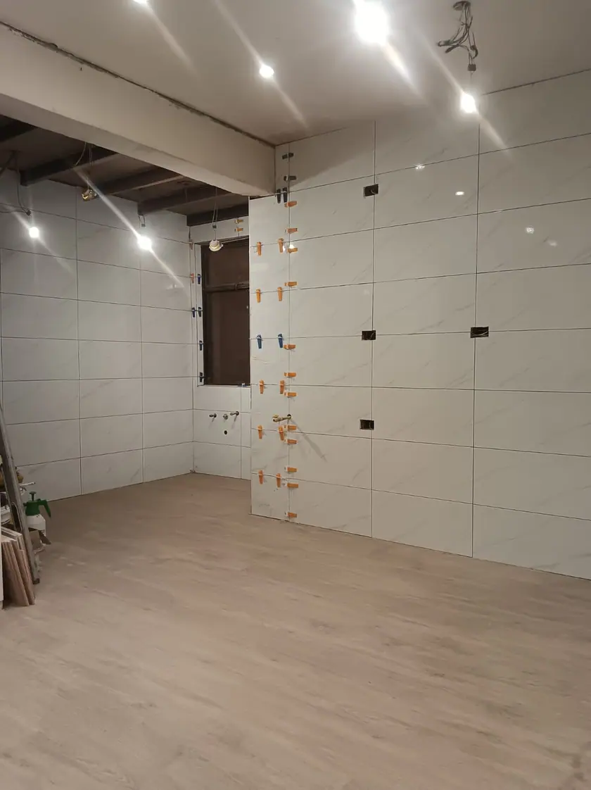 Revestimiento de gran formato en instalación, con las crucetas niveladoras aún puestas, sobre el piso laminado ya colocado.