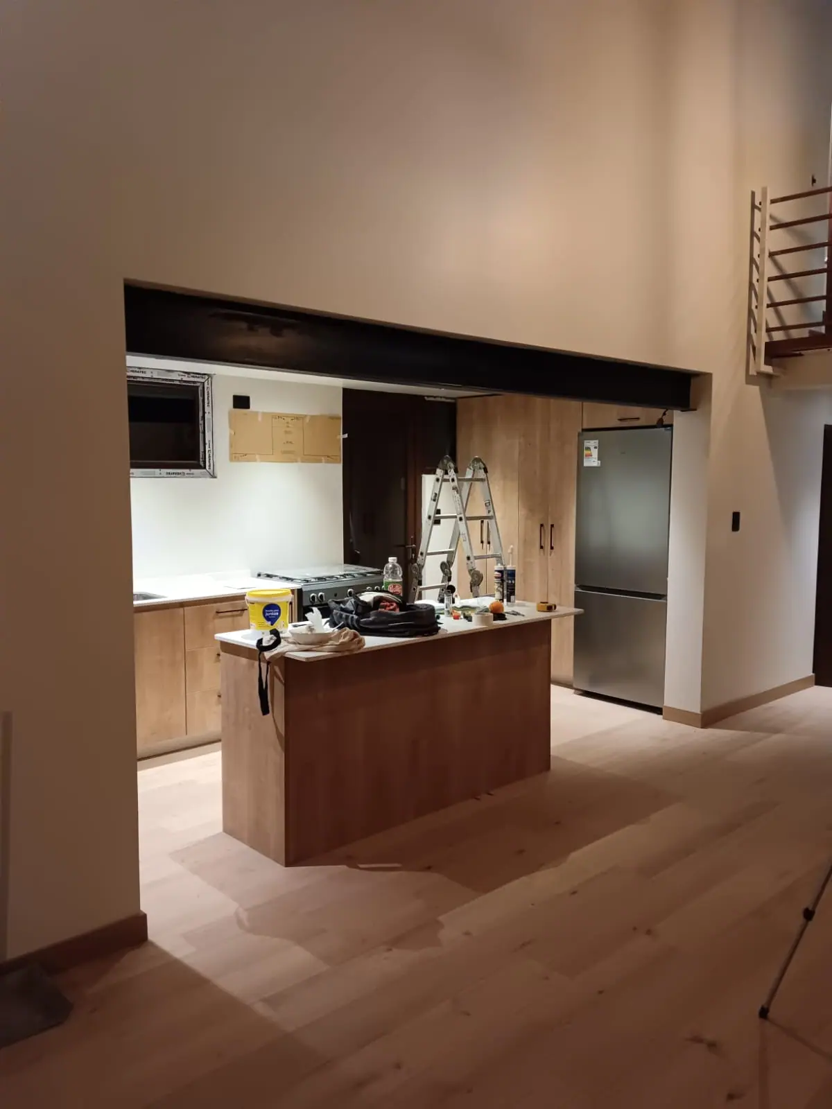 Cocina terminada e integrada al espacio contiguo, con isla de madera, pavimento continuo y la viga de acero a la vista sobre el vano.