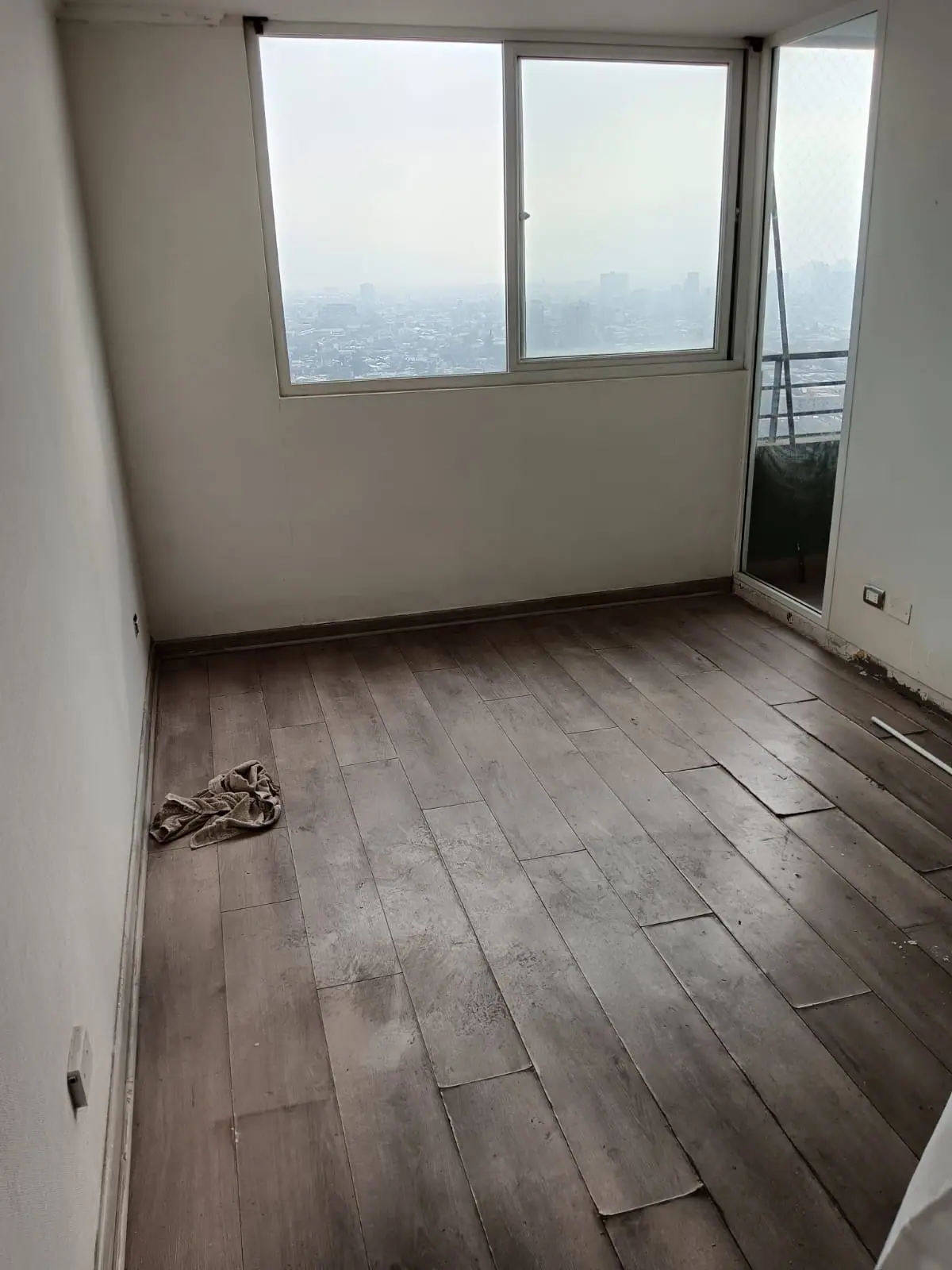 Recinto de un departamento en altura con piso flotante antiguo y tablas ya levantadas junto a la ventana.