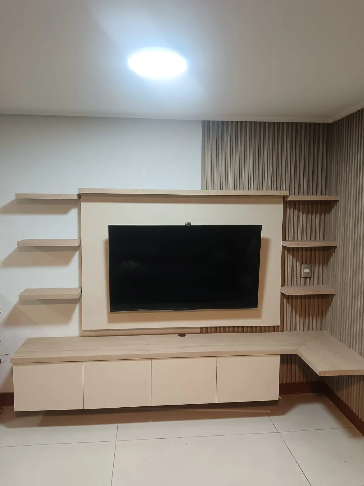 Conjunto terminado: panel de respaldo con listones verticales, televisor montado, repisas laterales y el mueble bajo continuo.