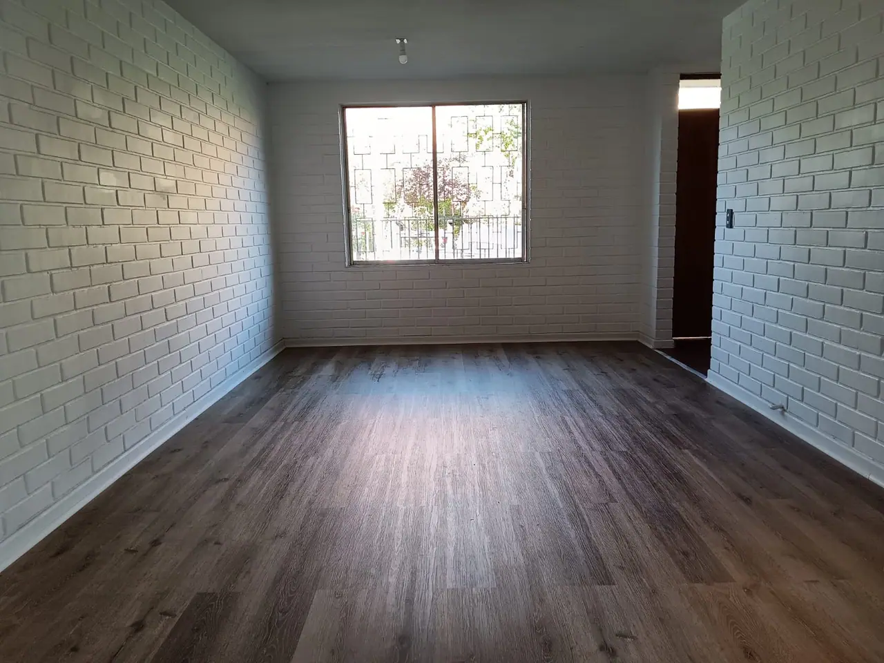 Recinto terminado con piso laminado, muros de albañilería pintados de blanco y la ventana con reja al fondo.